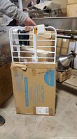 White metal expandable gate partially extended shown above its original packaging box.