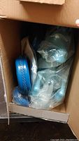 Cardboard box containing blue plastic parts wrapped in clear plastic bags, components of a Frozen themed ride on toy.