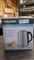 Front of the box showing the Kalorik brand electric kettle with details about stainless steel build, 1.7L capacity, boil dry protection, and cordless base.