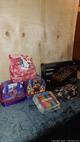 Full lot overview showing three backpacks stacked and foosball table box behind them, plus marker sets in front