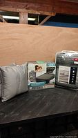 Queen air mattress in box, double bedding set, and two throw pillows displayed on table.