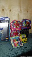 Photo showing 4 Westcott Titanium paper trimmers in packaging, 2 character-themed lunch bags including Trolls and Marvel Avengers, Paper Mate Flair pens, and glue sticks on a surface.