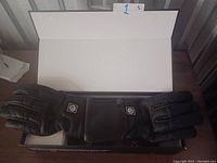 Photo of pair of black heated gloves laid flat with heating controller symbols visible on the gloves' top side.