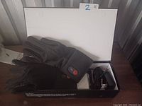 Photo of two black heated gloves with control modules and a charger with power cable placed on a flat surface.