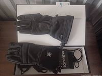 Photo shows five pairs of black heated gloves arranged with user guides visible, placed on a white surface with an indicator of quantity.