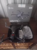 Photo of Holy Stone HS175D drone placed inside a black carrying case with original HS175D box behind it and two accessories in white plastic bags inside the case.