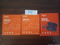 Photo of three unopened boxes: two M12 MPOW True Wireless Earbuds and one M9 MPOW True Wireless Earbuds box showing front design and branding.
