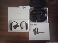 Photo of New Bee M50 Bluetooth headset inside a black zippered carrying case, box, charging cable, and two black alternate ear hooks, all arranged on a flat surface.