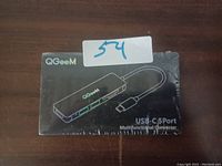 Photo of the QGeeM USB-C 5 Port Multifunctional Converter in sealed black packaging with product illustration and branding.