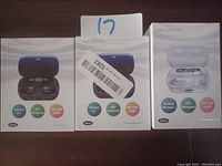 Three boxed sets of wireless earbuds with mini charging cases displayed. The boxes show the product in black and white colors, feature Bluetooth 5.1, IPX7 waterproof rating, built-in microphone, and 45ms low latency for gaming.