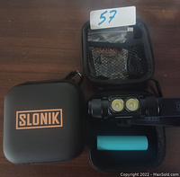 Photo shows contents of black Slonik-branded protective case with two dual LED headlamps, blue rechargeable battery, accessories in mesh pocket, and adjustable straps.