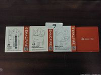 Photo showing three boxed Enacfire earbuds products: two A9 Active Noise Cancelling Earbuds and one E60 True Wireless Sport Earbuds box, plus one additional orange Enacfire box, all arranged side by side on a dark surface.