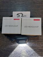 Two white product boxes labeled LED HEADLAMP with one headlamp powered on below them