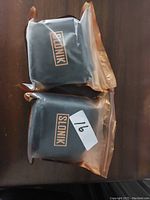 Two black items with Slonik branding, sealed in clear plastic bags placed on a wooden surface.