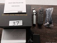 Smart mini projector with remote, tripod, charger, user manual, and HDMI cable laid out on table.