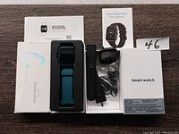 Photo showing the ID205L smart watch with blue band attached, black extra band, USB charging cable, and two user manuals.
