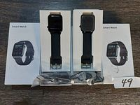 Two smart watches displayed on their packaging boxes, showing front of product with black straps and watch faces.