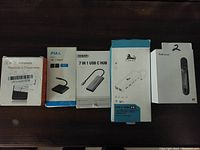Photo showing five boxed electronic accessories laid out in a row on a dark surface including USB-C hubs, wireless receiver, USB C adapter, and electronic lighter.