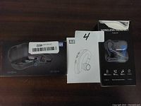 Photo showing four wireless Bluetooth headsets in their original packaging with charging cases visible in two boxes.