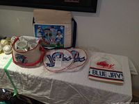 Overview of vintage Blue Jays collectibles including card, cooler bag, plates, mug, baseballs, and hat.