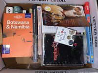 Box of assorted books including a Lonely Planet travel guide to Botswana & Namibia, The Button Book, Raptors notebook, and more.