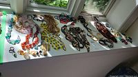 Wide view of costume jewelry collection laid out on a white surface by the window, showcasing multiple necklaces, bracelets, earrings, and brooches in various colors and styles.