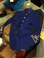 Blue double-breasted uniform coat laid out on a chair, showing gold trim and buttons, and black side panels