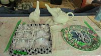 Set of seven clear art glass elephants in a black and white box, white ceramic elephant figurines, elephant teapot, and colorful Gien Jungle series plate with elephant motif.