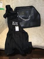 Black Toronto Raptors-themed purses and Adidas 'We the North' sweater coat on a light-colored patterned couch. Purse handles are wrapped in plastic protective covering.