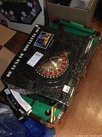 Mini roulette wheel box on top of mini pool table with cues and balls.