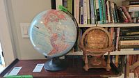 Full view of both globes on a table in front of a bookshelf.