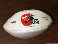Side of white football showing red helmet logo with running horse, '1992', 'Grey Cup Champion', and November 29, 1992 date.