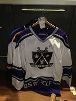 Front view of white and purple Los Angeles Kings signed hockey jersey over blue St Louis Blues jersey.