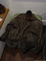 Brown leather men's coat laid flat showing full front with pockets and collar details.