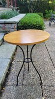 Round wood top with natural finish, showing full table from angled front view outdoors.