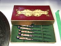 Original red and gold cardboard box labeled “Royal Crown Derby China” with green felt interior holding six porcelain-handled blades
