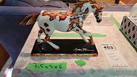 Side view of ceramic horse figurine on black base showing painted designs and overall size tape