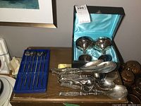 Overview of all items on table: goblets in case, set of long spoon iced tea spoons in blue velvet case, and multiple silver serving spoons