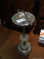 Full view of vintage ashtray stand showing metal top tray with branch handle, ribbed metal pole, onyx decorative discs, and detailed metal base.