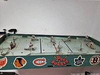 Top view of the 1950s hockey game with player figures arranged on painted rink surface featuring NHL team logos on the side panel.