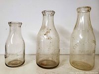 Three vintage Ottawa Dairy glass milk bottles on white background showing varying heights and embossed text.