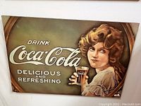 Photo of the vintage Coca-Cola picture showing a young woman holding a glass of Coca-Cola with slogan text.