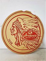 Front view of round vintage cardboard sign with Iroquois Beer & Ale branding and Native American chief profile.
