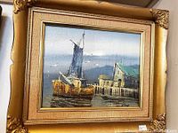 Image of oil painting depicting a yellow sailboat docked near waterfront buildings with a cloudy sky background. The painting is framed in a gold-colored ornate frame.