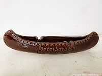 Front side view of the brown glazed ceramic ashtray shaped like a canoe with 'Peterborough' embossed.