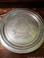 Front of pewter plate showing embossed sailing ship design.