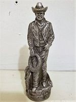 Front view of the pewter cowboy statue showing detailed clothing and lasso held in hand.