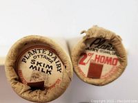 Close-up of the tops of the two cylindrical cardboard tubes showing vintage milk tabs labeled '2% Homo' and 'Skim Milk' from Plante Dairy Ottawa.