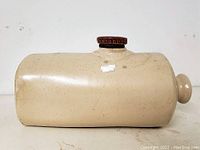 Side view of the pottery foot warmer showing smooth beige ceramic surface and dark brown metal screw cap on top.