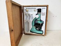 Full view of the Tasco Deluxe microscope set inside the wooden case with foam inserts holding the microscope and accessories.
